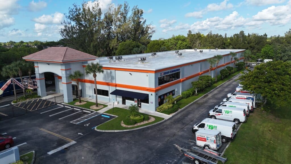Aerial view of U-Haul self-storage facility with white building, orange trim, flat roof, and rental trucks parked outside.