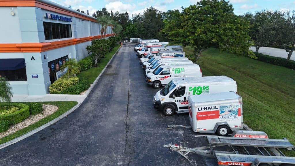 Row of white U-Haul rental trucks parked outside self-storage facility building.
