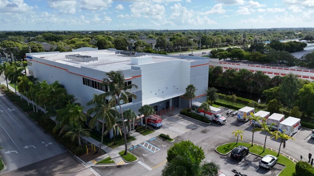 Aerial view of modern white self-storage facility with orange accents, palm trees, and parking lot.