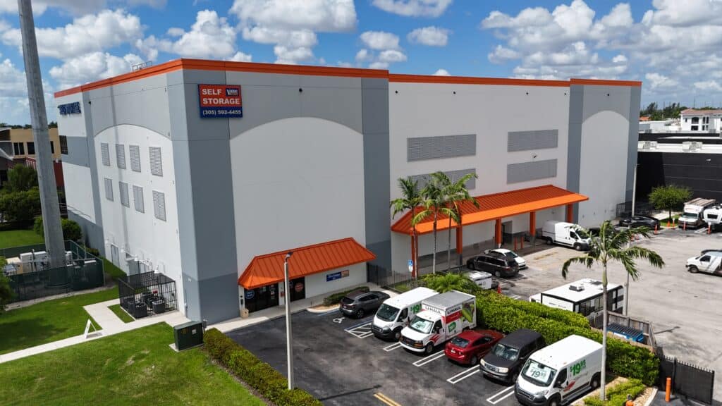 Exterior of Value Store It self-storage facility with orange and gray metal building, covered loading area, and parked vehicles.