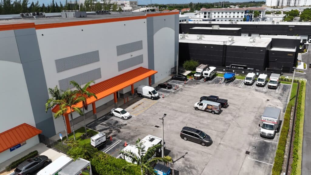Aerial view of Value Store It facility with orange awning, parking lot, and adjacent black warehouse building in sunny residential area.