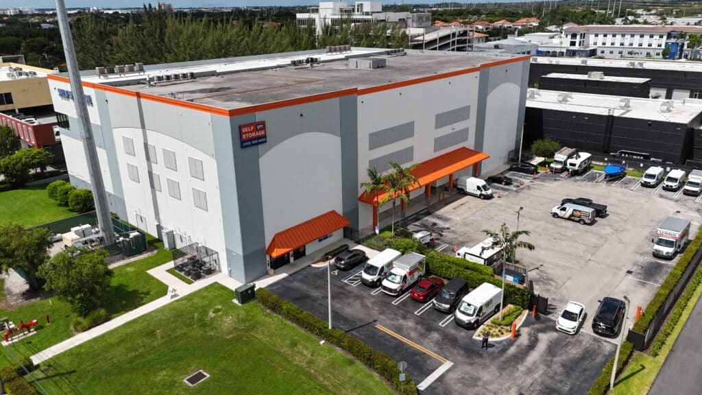 Aerial view of Value Store It self-storage facility with white building, orange trim, parked vehicles, and landscaping.
