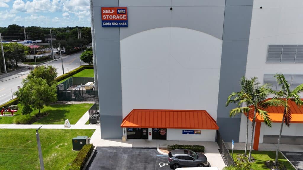 Exterior view of Value Store It self-storage facility with orange awning and entrance, palm trees, parking area visible.